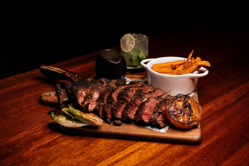 Tomahawk-steak skåret opp på fjøl med søtpotetfries og mojito